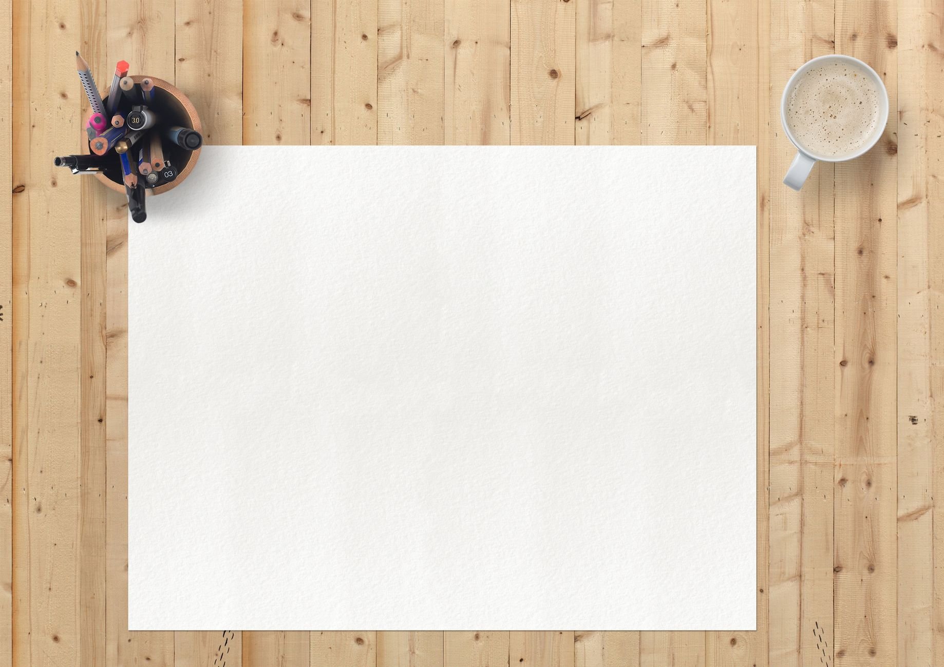 Flat lay of art supplies, blank paper, and coffee on a wooden desk — a creative professional's workspace