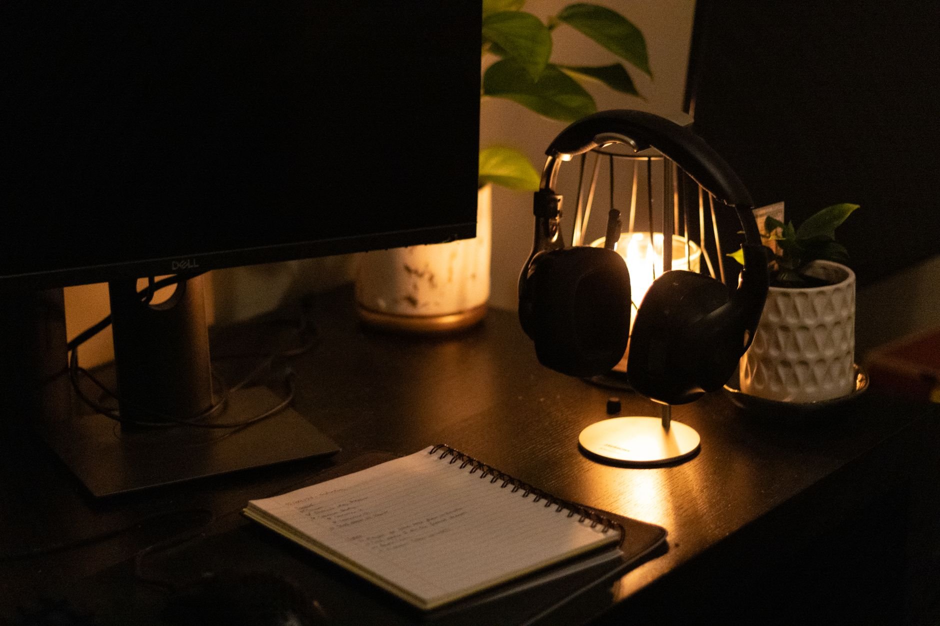 Warmly lit minimal desk with monitor, headphones, and notebook — a refined creative workspace
